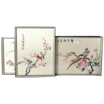 A group of Oriental embroideries on silk, various birds pictured resting on branches in bushes, with