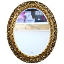 A large wooden oval wall-hanging bevel-edge mirror, in ornate giltwood frame, 76cm x 63cm