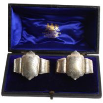 A pair of Edward VII engraved silver napkin rings, standing on ball feet, in fitted box, retailed by