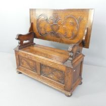 An early 20th century carved oak monk's bench, with carved and panelled decoration, lifting seat and