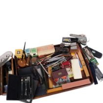 An oak tray with a large quantity of desk items, including fountain pens, hole puncher, rulers,