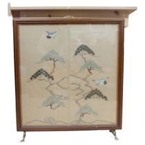 A mahogany-framed fire screen with brass mounts, inset Oriental embroidery depicting flying cranes