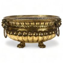 A 19th century oval brass jardiniere, with cast lion mask ring handles and lion paw feet, length
