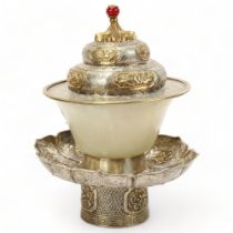 A Chinese jade ceremonial cup, in unmarked chased parcel-gilt white metal lotus flower design stand,