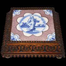 A Delft polychrome pottery tile depicting a farmer's wife, in carved wood stand with brass feet,