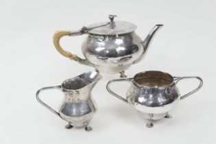 Arts and Crafts silver composite three piece tea service, the lidded hammered teapot by William