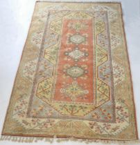 Turkish woollen carpet, having a salmon pink field with wide borders of yellow, blue and mustard,