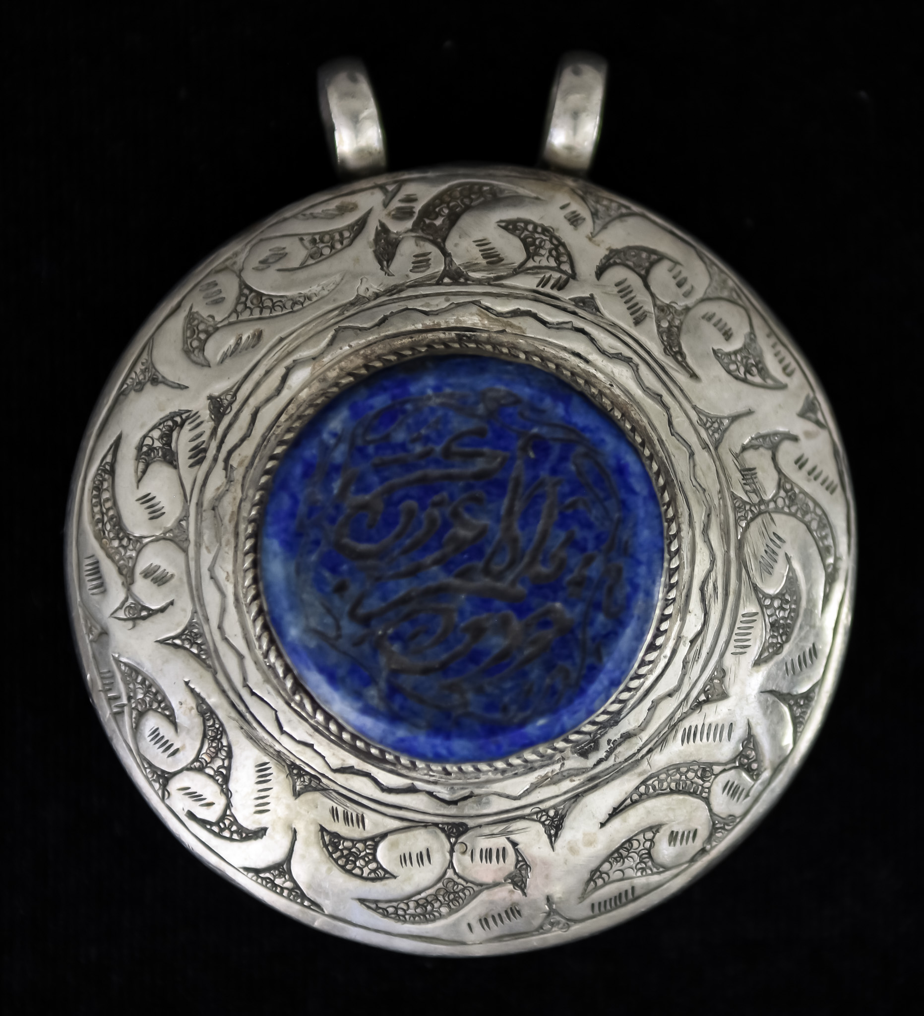 An Arabic Pendant, 20th Century, silvery metal, set with a centre Lapis Lazuli panel, 25mm in