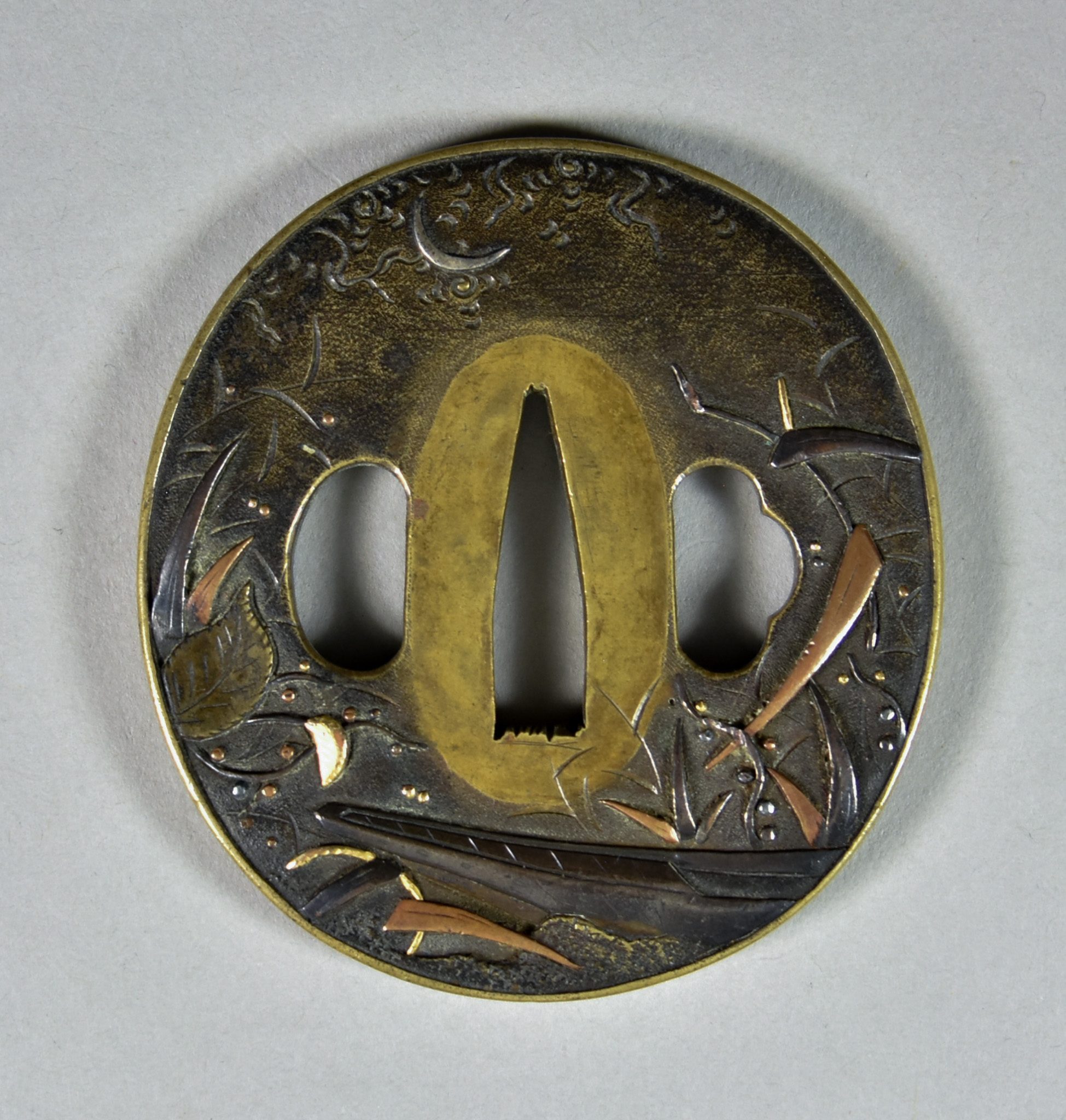 A Japanese Tsuba, Sentoku Naga Maru-gata, depicting a boat amongst reeds under a crescent moon,