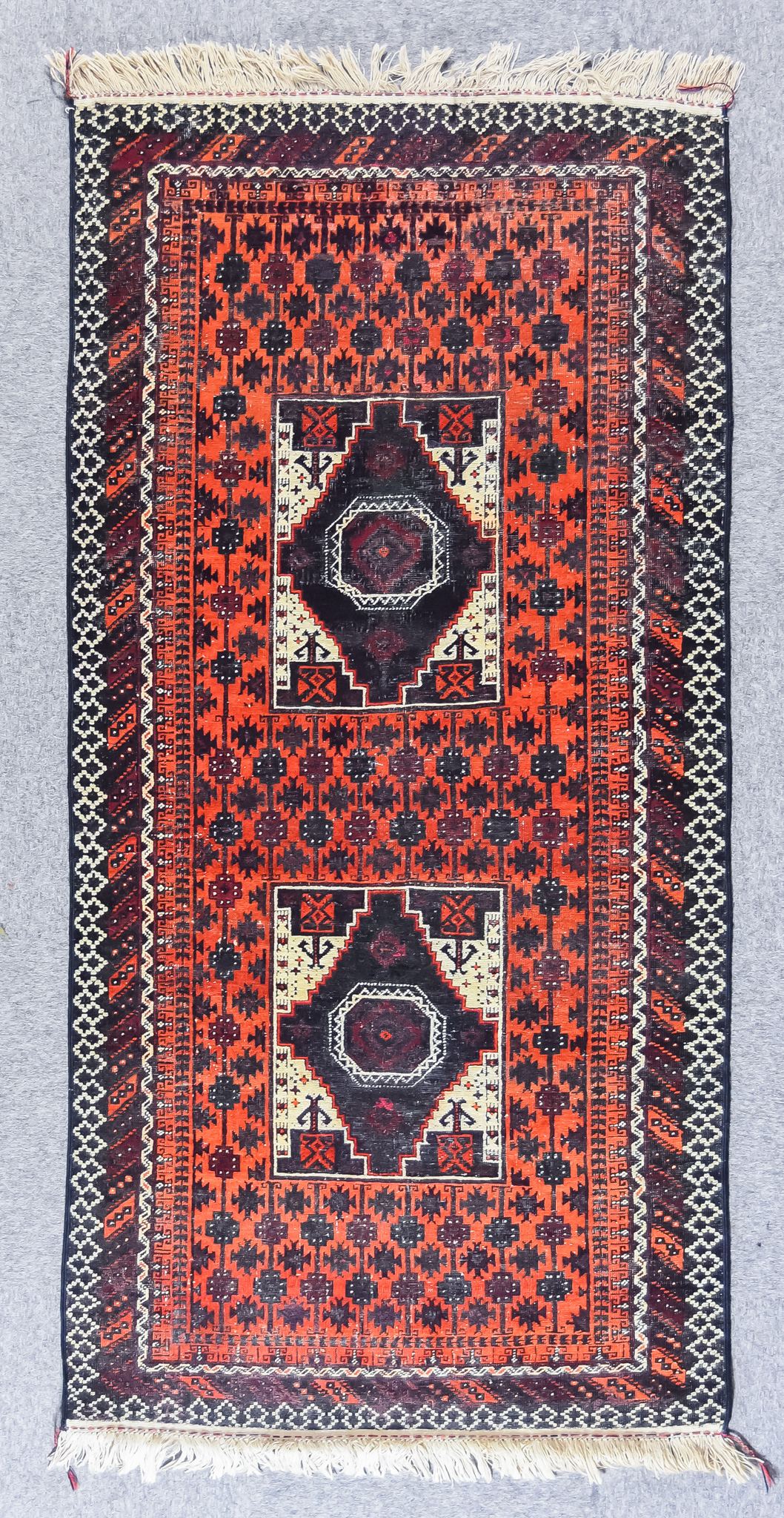 An Early 20th Century Turkmen Rug woven in colours of terracotta, ivory, navy blue and wine, with