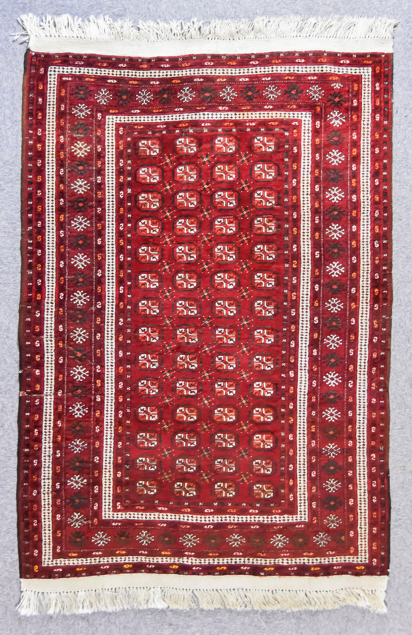 An Early 20th Century Turkmen Rug, woven in colours of ivory, navy blue and wine, with four rows