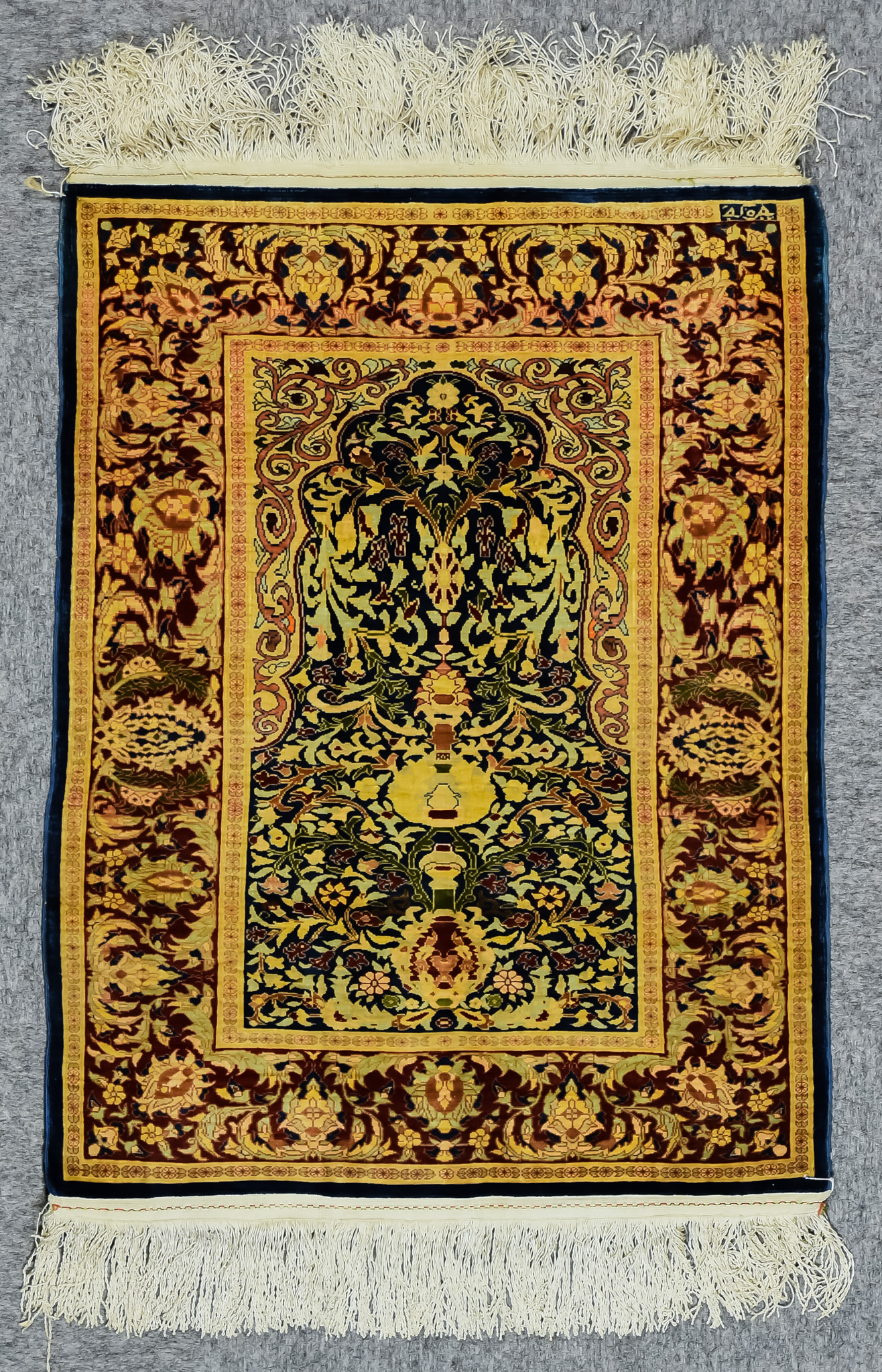 A Qum Silk Prayer Rug, woven in colours, of fawn, navy blue and wine, with a central mihrab filled