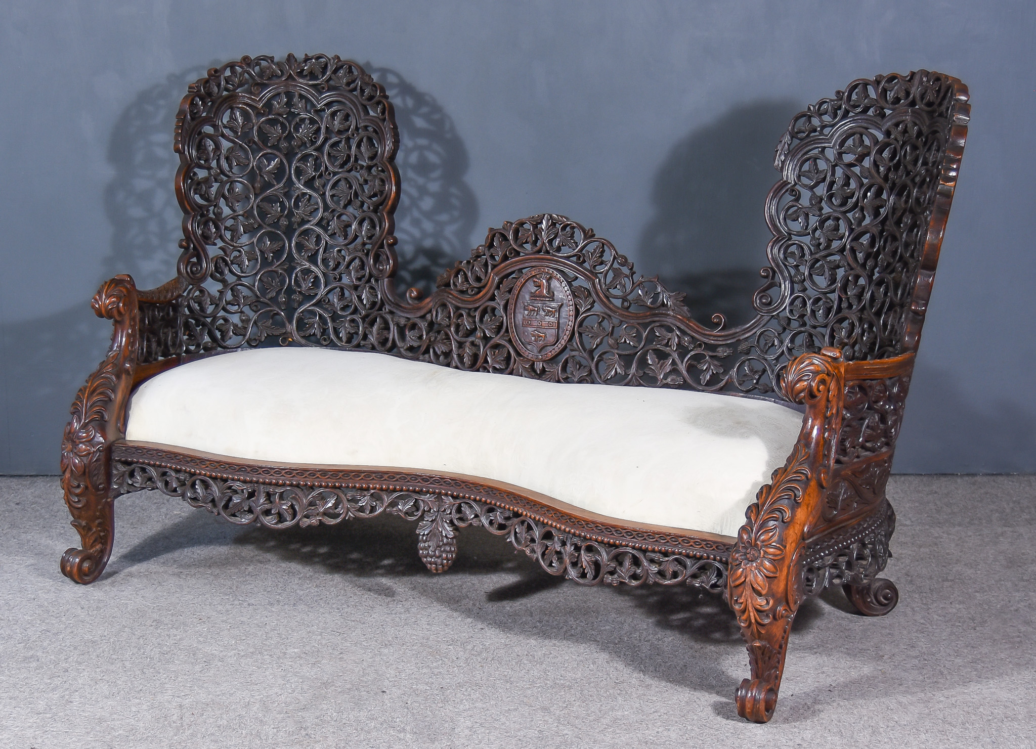 A 19th Century Burmese Hardwood Love Seat, the shaped back fretted and carved with leaf,