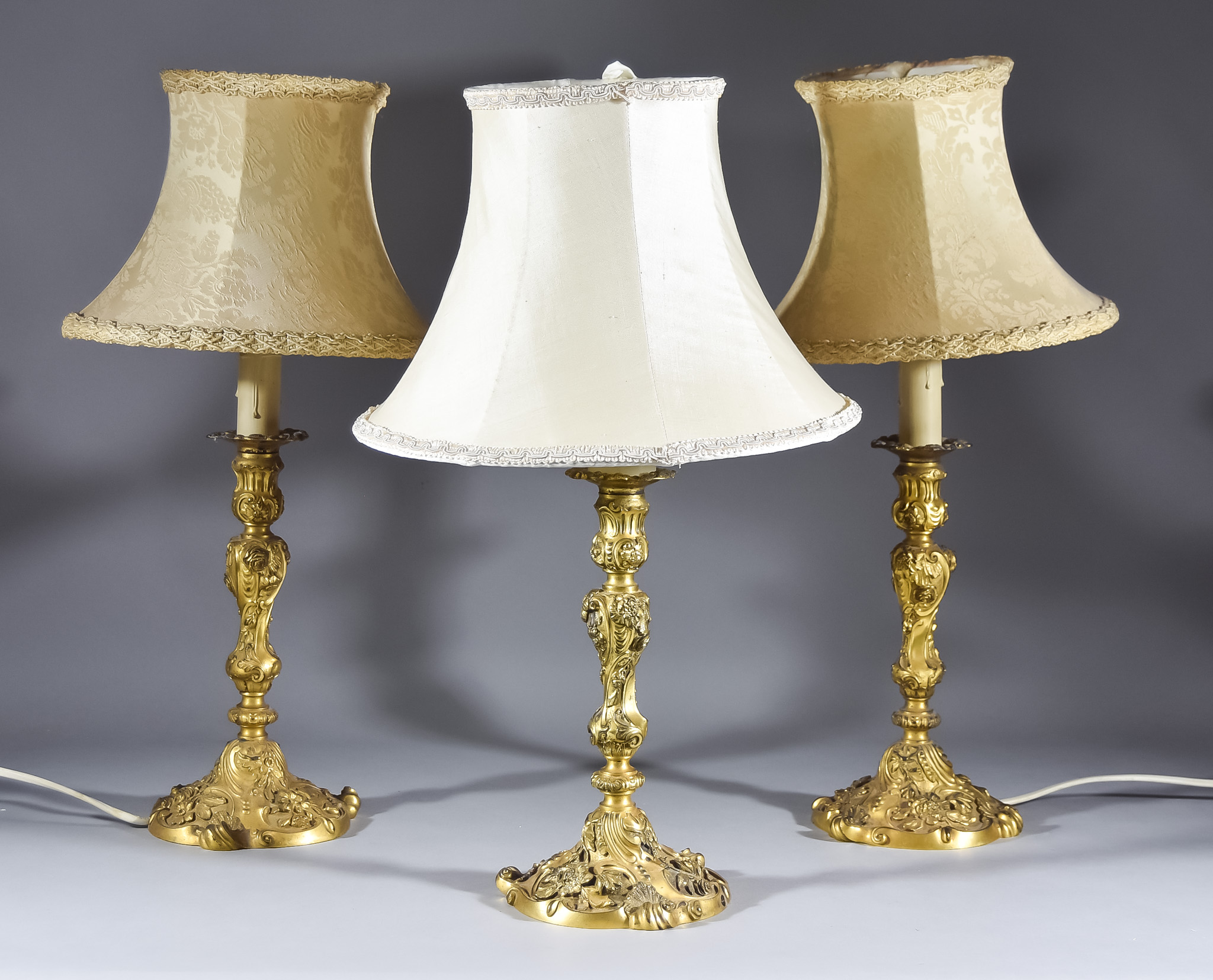 Three French Gilt Brass Candlesticks of Louis XV Design chased and cast with floral leaf scroll