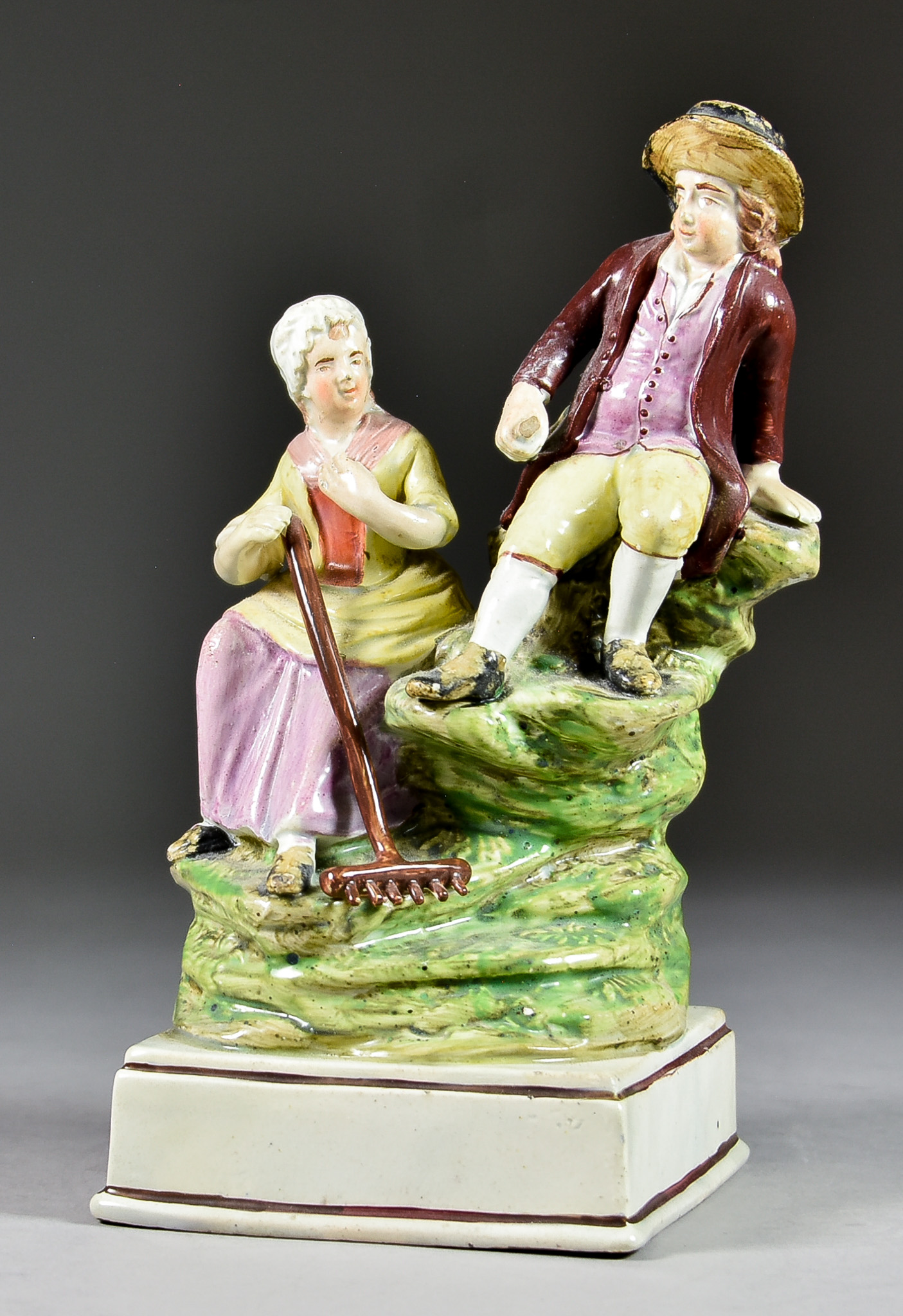 An English Pearlware Pottery Group, Early 19th Century, of seated rustic figures of a man and woman,