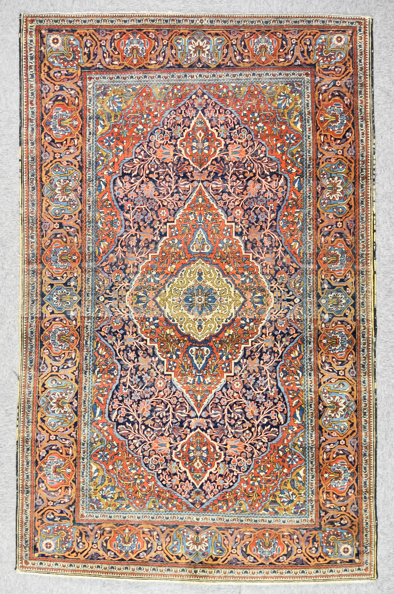 An Antique Kirman Rug, woven in colours of navy blue, terracotta, fawn and ivory, the bold central