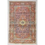 An Antique Kirman Rug, woven in colours of navy blue, terracotta, fawn and ivory, the bold central