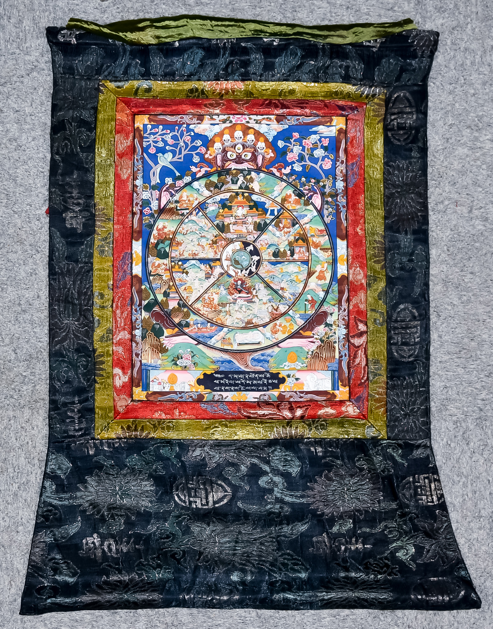 A Tibetan Tanka, painted on silk with circular segmented panel of various figures, mythical beast,