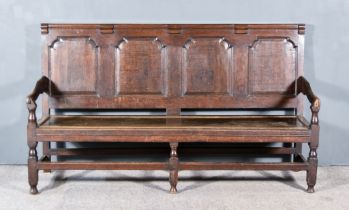 An 18th Century Oak Settle, with four fielded panel back, scroll arms, wooden seat, on square legs