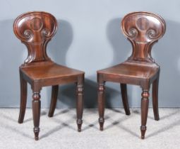 A Pair of George III Mahogany Hall Chairs, the shaped backs with leaf scroll moulding, plain wood