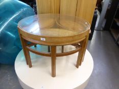 A TEAK CIRCULAR COFFEE TABLE WITH GLASS TOP, HAVING THREE LOZENGE SHAPED NESTING TABLES