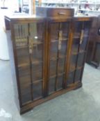 AN ART DECO OAK STEP-TOP BOOKCASE, HAVING THREE GLAZED PANEL DOORS WITH SMALL CENTRAL DRAWER