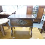 A CARVED OAK OBLONG BOX STOOL WITH HINGED LID ON TRESTLE END SUPPORTS