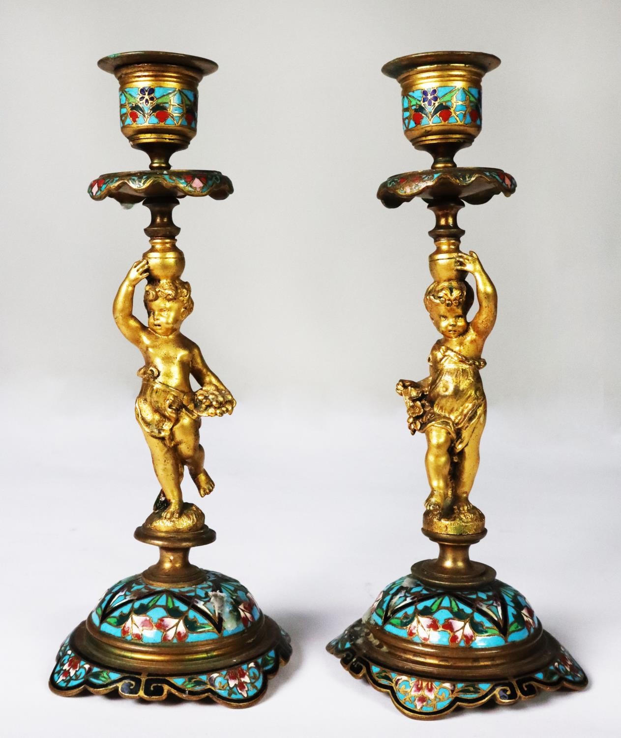 PAIR OF TWENTIETH CENTURY ORMOLU AND CHAMPLEVÉ FIGURAL CANDLESTICKS, each modelled as a cherub,