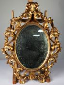 FLORENTINE STYLE CARVED GILTWOOD WALL MIRROR, the oval, mirrored plate within a beaded surround