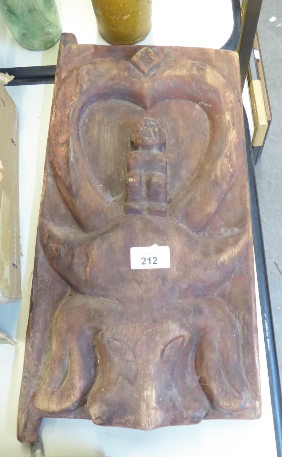 AN ETHNIC CARVED SOFTWOOD DOOR WITH SMALL FIGURES ON THE HEAD OF A BUFFALO, 16” X 9 ½”