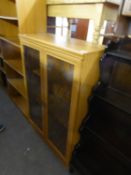 A WOOD FINISH DWARF BOOKCASE, ENCLOSED BY TWO GLAZED DOORS, 2’8” WIDE