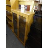 A WOOD FINISH DWARF BOOKCASE, ENCLOSED BY TWO GLAZED DOORS, 2’8” WIDE