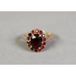 9ct GOLD GARNET OVAL CLUSTER RING, set with a centre oval garnet and surround of fourteen small
