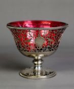 GEORGE V PIERCED SILVER PEDESTAL SUGAR BASIN WITH RUBY GLASS LINER, of flared form, the foliate