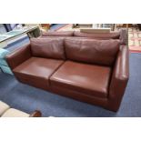 A STYLISH THREE SEATER SOFA, HAVING TWO LOOSE BASE AND BACK CUSHIONS, COVERED IN BROWN LEATHER