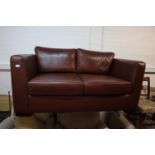 A STYLISH TWO SEATER SOFA, HAVING TWO LOOSE BASE AND BACK CUSHIONS, COVERED IN BROWN LEATHER (
