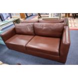 A STYLISH THREE SEATER SOFA, HAVING TWO LOOSE BASE AND BACK CUSHIONS, COVERED IN BROWN LEATHER