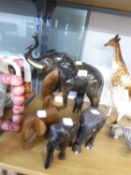 A LARGE CERAMIC MODEL OF AN ELEPHANT WITH TRUNK RAISED; TWO CARVED EBONY ELEPHANTS AND THREE OTHER