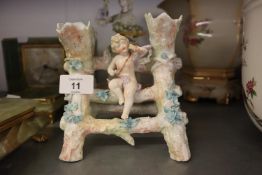 A CONTINENTAL PORCELAIN FLOWER RECEIVER IN THE FORM OF A CHERUB ON A STILE (BROKEN)
