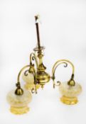 EARLY TWENTIETH CENTURY BRASS THREE LIGHT ELECTROLIER, with scroll arms and amber glass shades