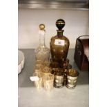 A SMOKED GLASS AND GILT DECORATED DECANTER AND MATCHING TOTS AND A CUT GLASS DECANTER AND MATCHING