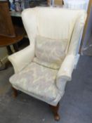 A WINGED FIRESIDE ARMCHAIR, WITH CREAM FABRIC LOOSE COVER, CABRIOLE FRONT SUPPORTS