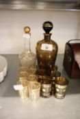 A SMOKED GLASS AND GILT DECORATED DECANTER AND MATCHING TOTS AND A CUT GLASS DECANTER AND MATCHING