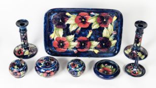 MOORCROFT PANSY PATTERN SEVEN PIECE TUBE LINED POTTERY DRESSING TABLE SET, on inky blue grounds,