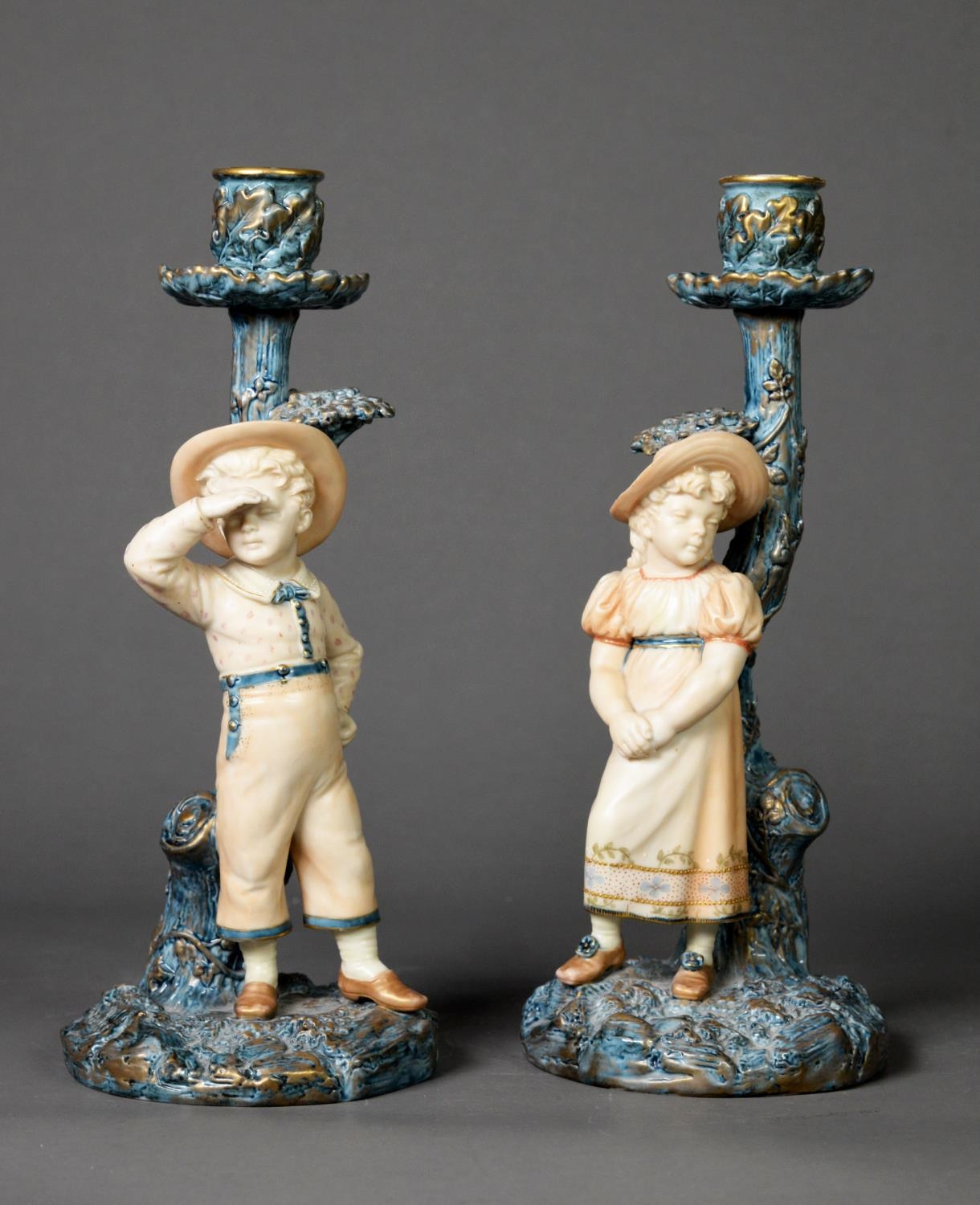 LATE NINETEENTH CENTURY PAIR OF ROYAL WORCESTER PORCELAIN FIGURAL CANDLESTICKS each painted in muted