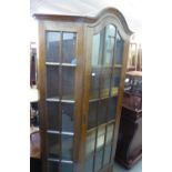 A LARGE OAK DISPLAY CABINET, WITH LARGE ASTRAGAL GLAZED DOME-TOP DOOR AND CANTED SIDES AND SINGLE