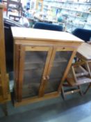 A PINE BOOKCASE WITH TWO GLAZED DOORS ENCLOSING TWO WOODEN SHELVES, ON PLINTH BASE