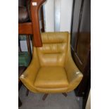 A REVOLVING TUB SHAPED LOUNGE EASY CHAIR, COVERED IN MUSTARD COLOURED VINYL ON WOODEN FOUR SPUR BASE