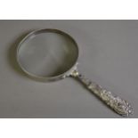 ‘GERMAN SILVER’ FRAMED LARGE MAGNIFYING GLASS WITH FOLIATE SCROLL EMBOSSED AND FILLED HANDLE,