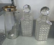 A PAIR OF CUT GLASS SQUARE SHAPED DECANTERS AND STOPPERS AND A CLEAR GLASS TALL JUG WITH SILVER